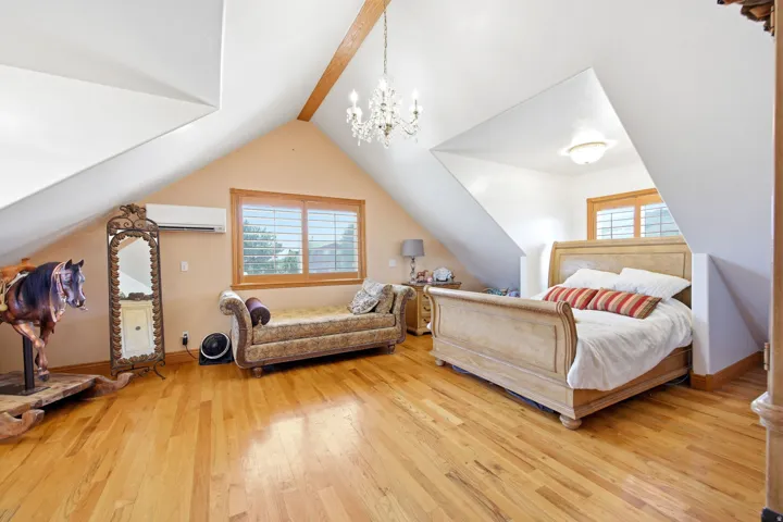 Main home - Expansive master bedroom featuring pitched ceilings, wood-finish flooring, a wood beam accent, a chandelier, and a window with plantation shutters
