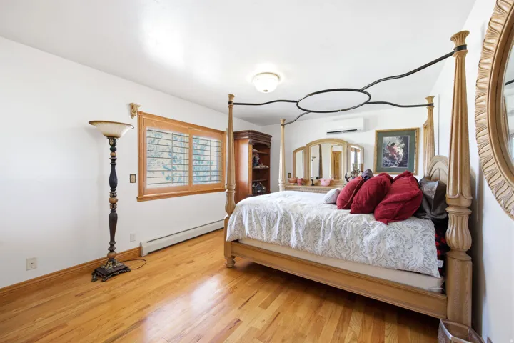 Main home - Hardwood flooring and white walls complement this room featuring a window with wood plantation shutters, a ceiling-mounted light fixture, and an air conditioning unit