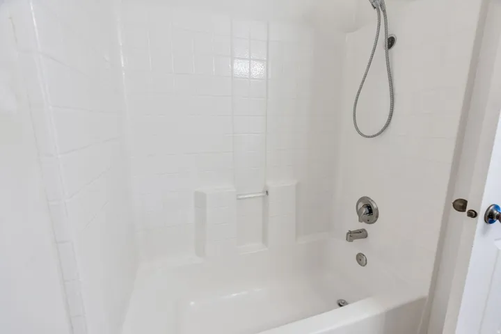 White tiled shower-over-tub combination featuring a built-in soap dish, chrome fixtures, and a handheld showerhead