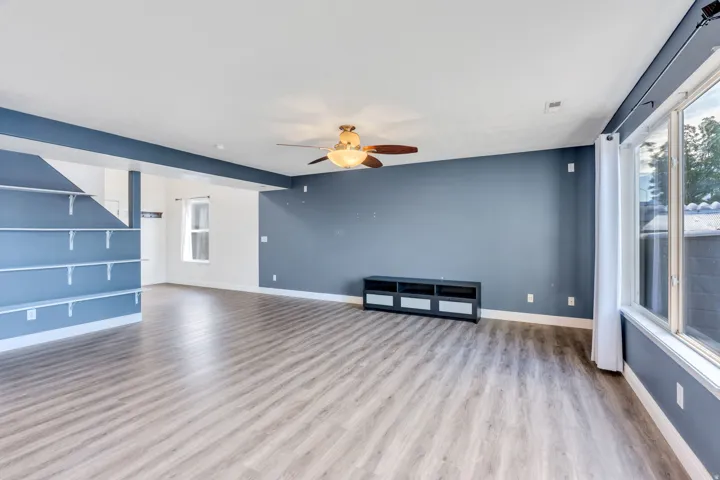 Spacious interior featuring wood-finish flooring, a ceiling fan with integrated lighting, and built-in shelving