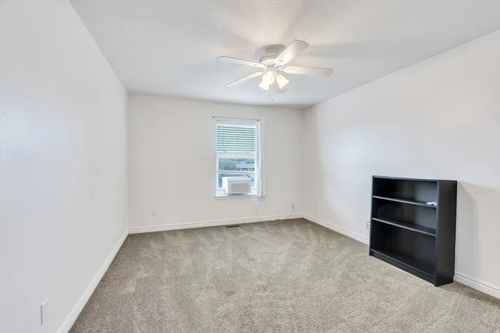 Carpeted room featuring a ceiling fan, white walls, and window with blinds