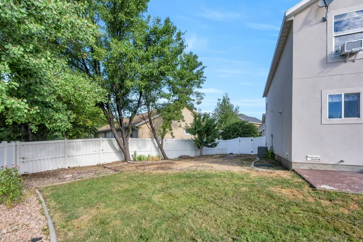 Spacious backyard featuring a manicured lawn, established trees, and a white privacy fence