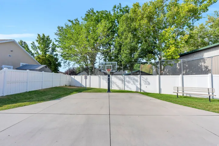 Paved court with a basketball hoop, surrounded by a white privacy fence
