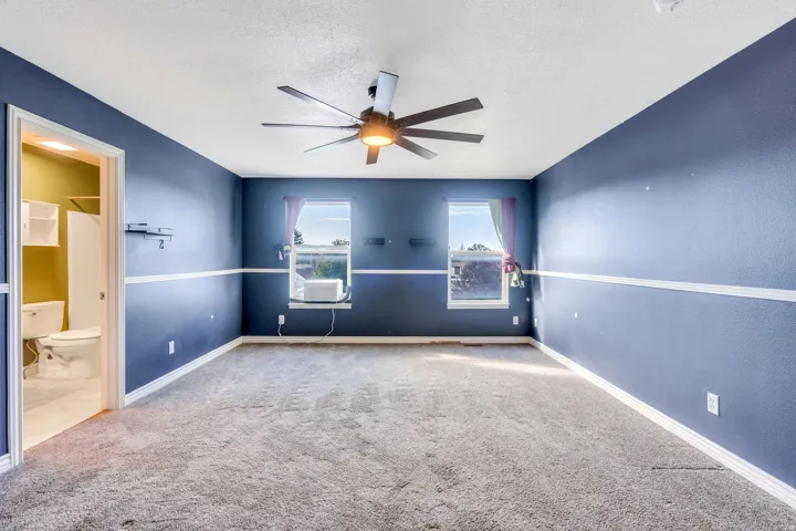 Spacious room featuring broadloom carpeting, two windows, and a ceiling fan