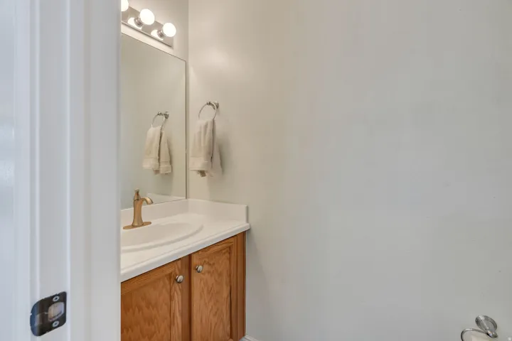 White countertop vanity with wood-finish cabinetry, a single basin sink, and a gold-tone faucet