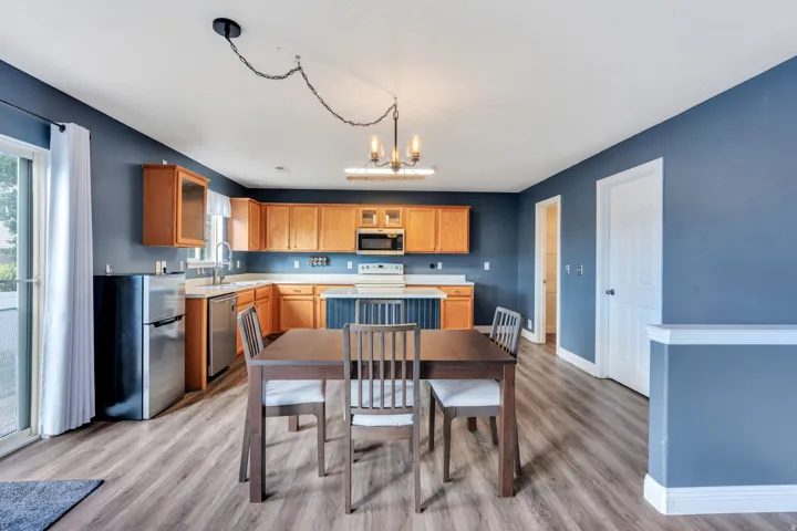Open-concept kitchen and dining area featuring wood-finish flooring, warm-toned cabinetry, a built-in microwave, and stainless steel appliances