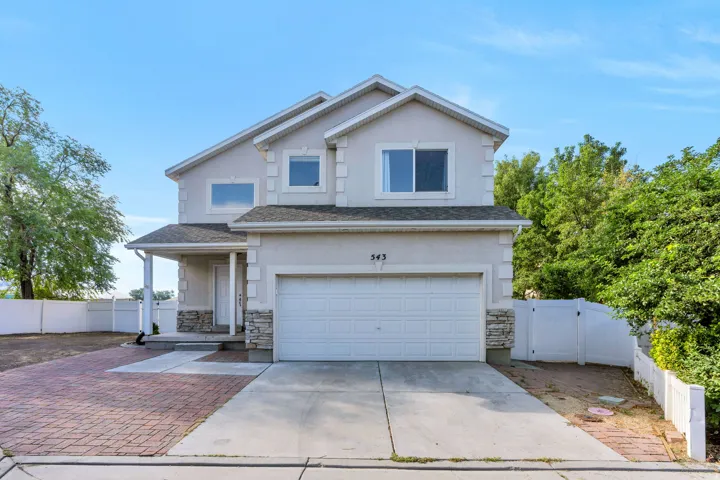 Two-story stucco exterior featuring stone accents, an attached garage, a covered front porch, and a paved driveway with brick-finish detailing