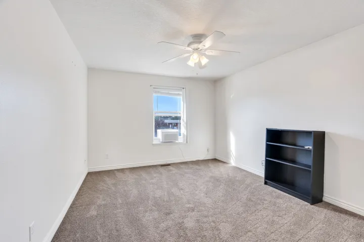 Carpeted room with white walls, a ceiling fan, and a window with an air conditioning unit