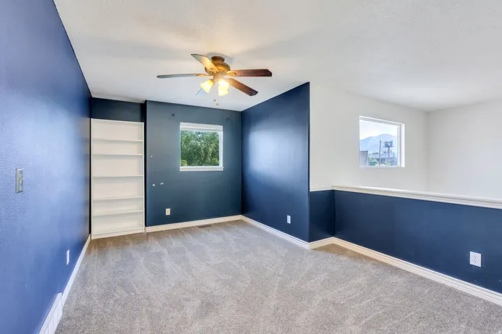 Carpeted room featuring a ceiling fan with light fixture, built-in shelving, and multiple windows