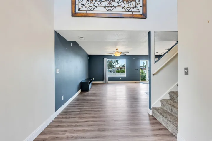 Open-concept living space with wood-finish flooring, a contemporary ceiling fan with integrated lighting, and multiple windows providing natural light