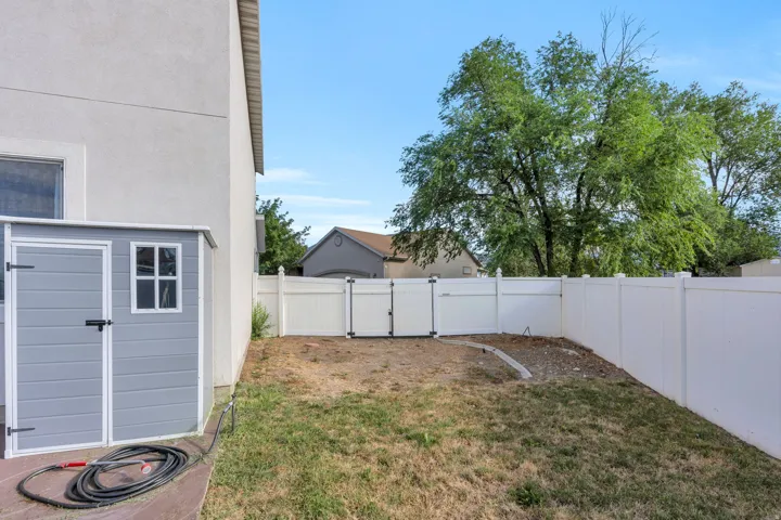 Fully fenced backyard featuring a gray storage shed with a white trim window, a double-gate entry, and a stucco-style exterior wall