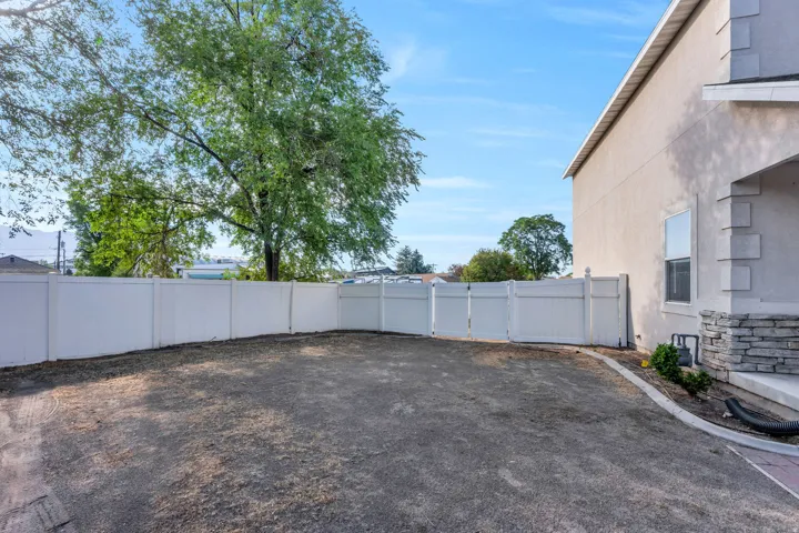 Spacious side yard featuring a white privacy fence, mature trees, and a gravel surface