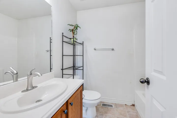 Bathroom featuring a single vanity with a white countertop and an integrated sink, brushed nickel faucet, wood-finish cabinetry, a toilet, and a bathtub with white subway tile surround