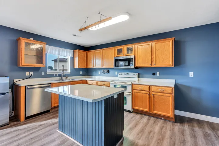 Kitchen featuring wood-finish flooring, a central island with a light-toned countertop, wood cabinetry, stainless steel dishwasher, and built-in microwave