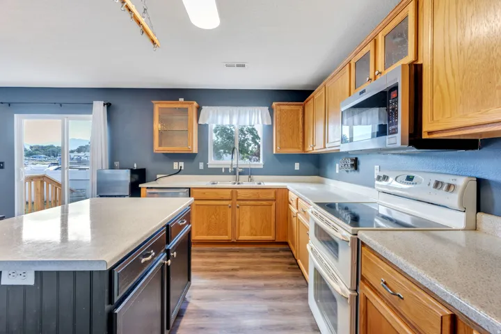 Kitchen featuring a central island with a solid surface countertop, wood-finish flooring, light wood cabinetry, a built-in microwave, and a glass sliding door