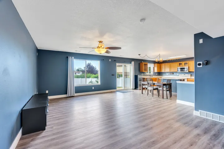 Open-concept living space featuring wood-finish flooring, a ceiling fan with integrated lighting, and a sliding glass door