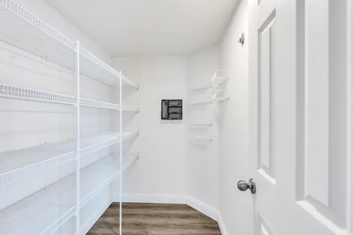 Dedicated utility room featuring extensive wire shelving, durable wood-finish flooring, white baseboards, and a paneled interior door