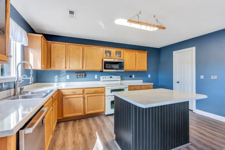 Kitchen featuring light wood cabinetry, white countertops, stainless steel sink, and an integrated island with a light-colored countertop