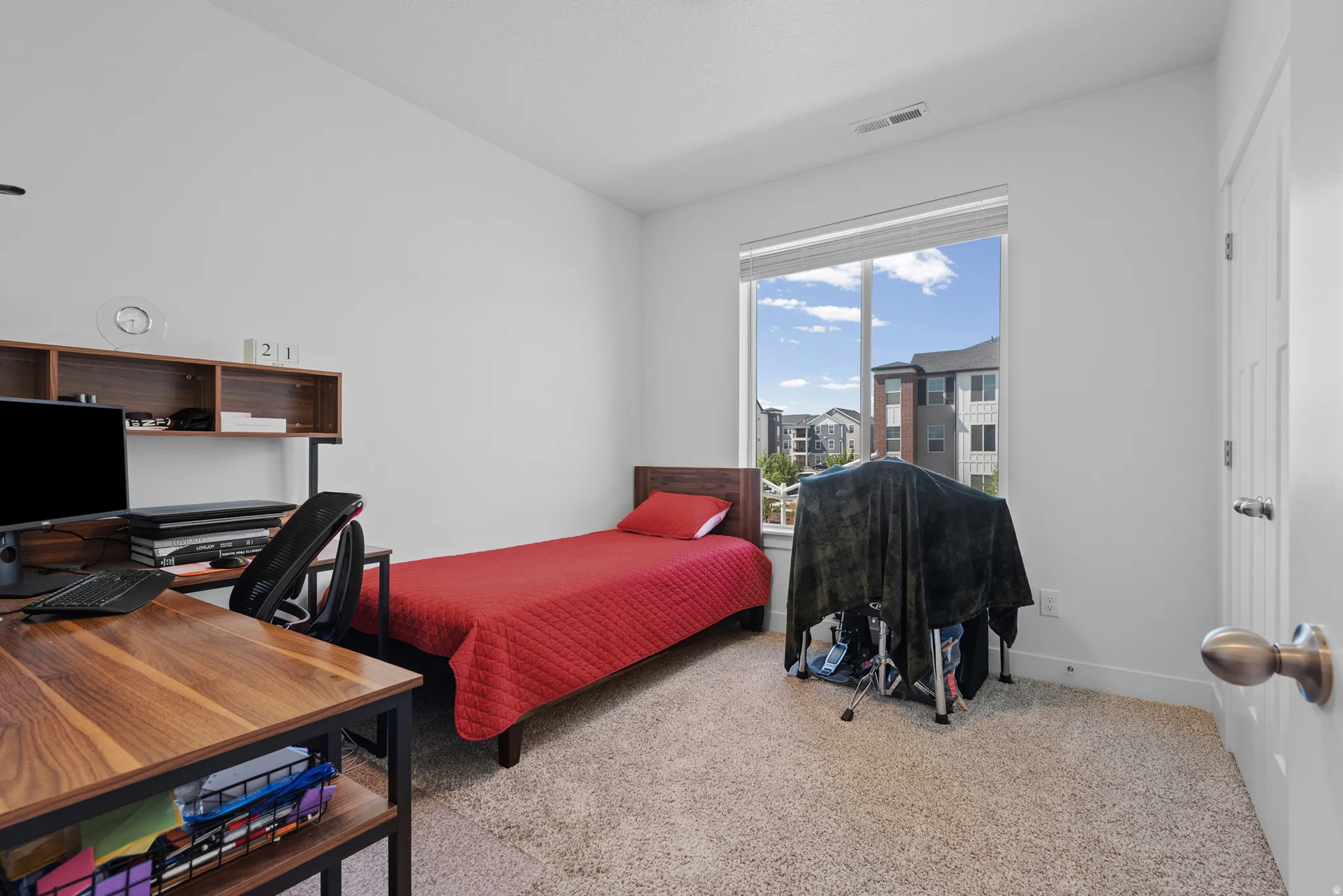 Light-filled room featuring a large window, neutral carpeting, and a white paneled door with brushed metal hardware