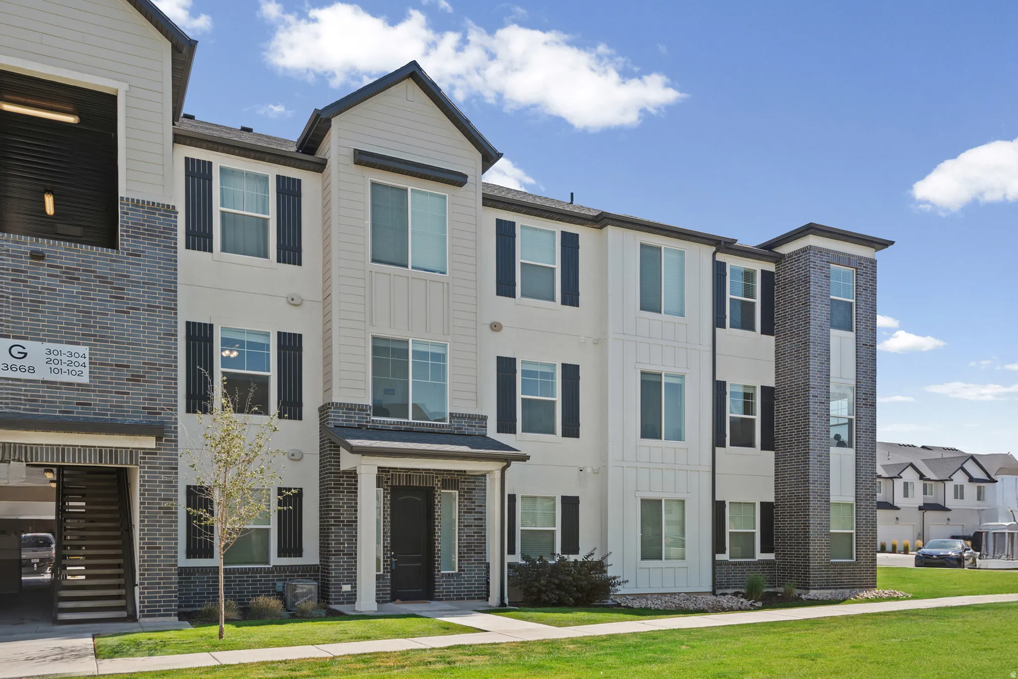 Contemporary multi-story facade featuring light-colored siding, dark brick accents, a gabled roofline, columned entry, and dark window shutters