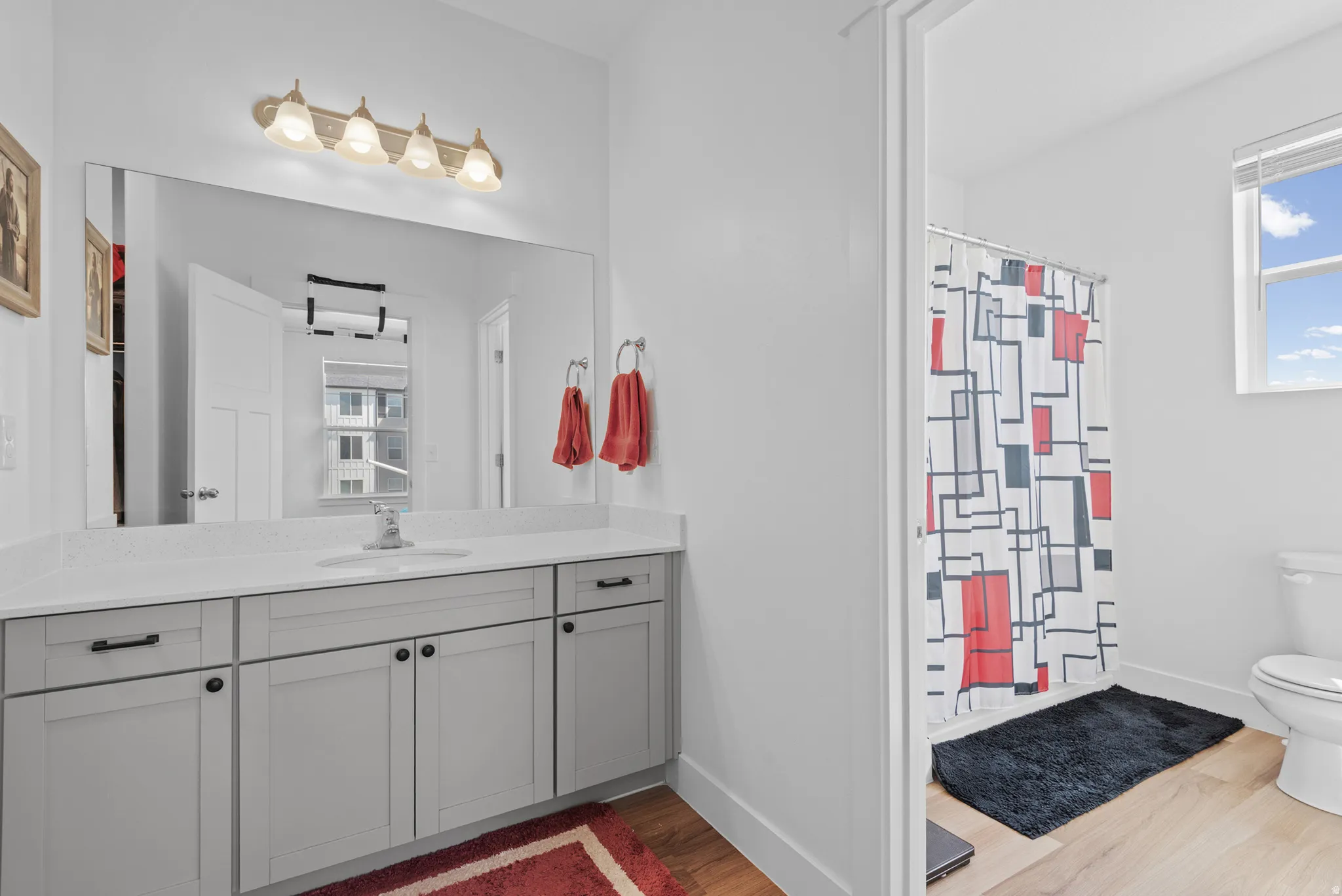 Bright bathroom featuring a light-colored vanity with a white countertop and undermount sink, ample storage cabinetry with dark hardware, a large wall-mounted mirror, and a wall-mounted light fixture