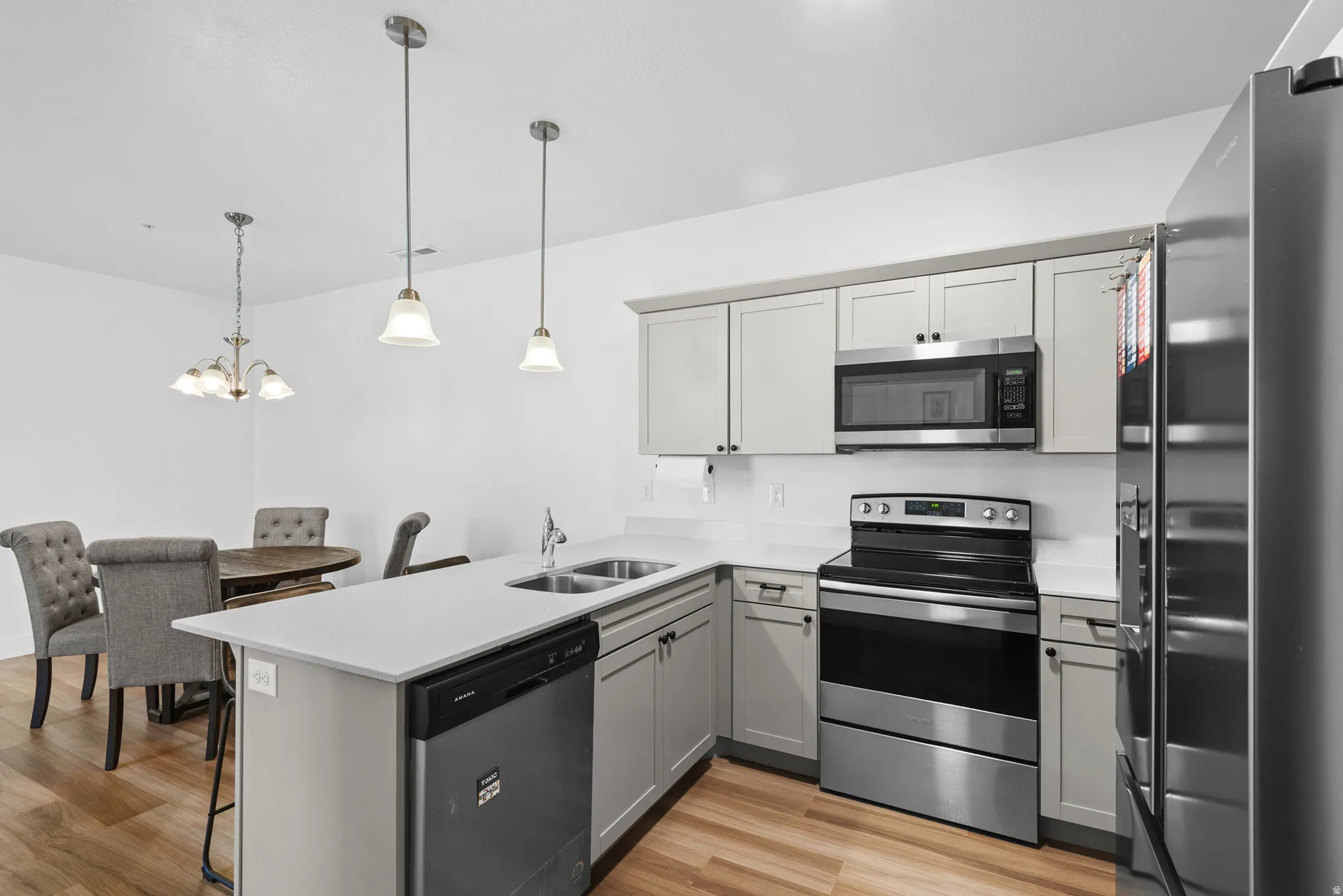 Modern kitchen featuring light gray cabinetry, stainless steel appliances, white countertops, and wood-finish flooring