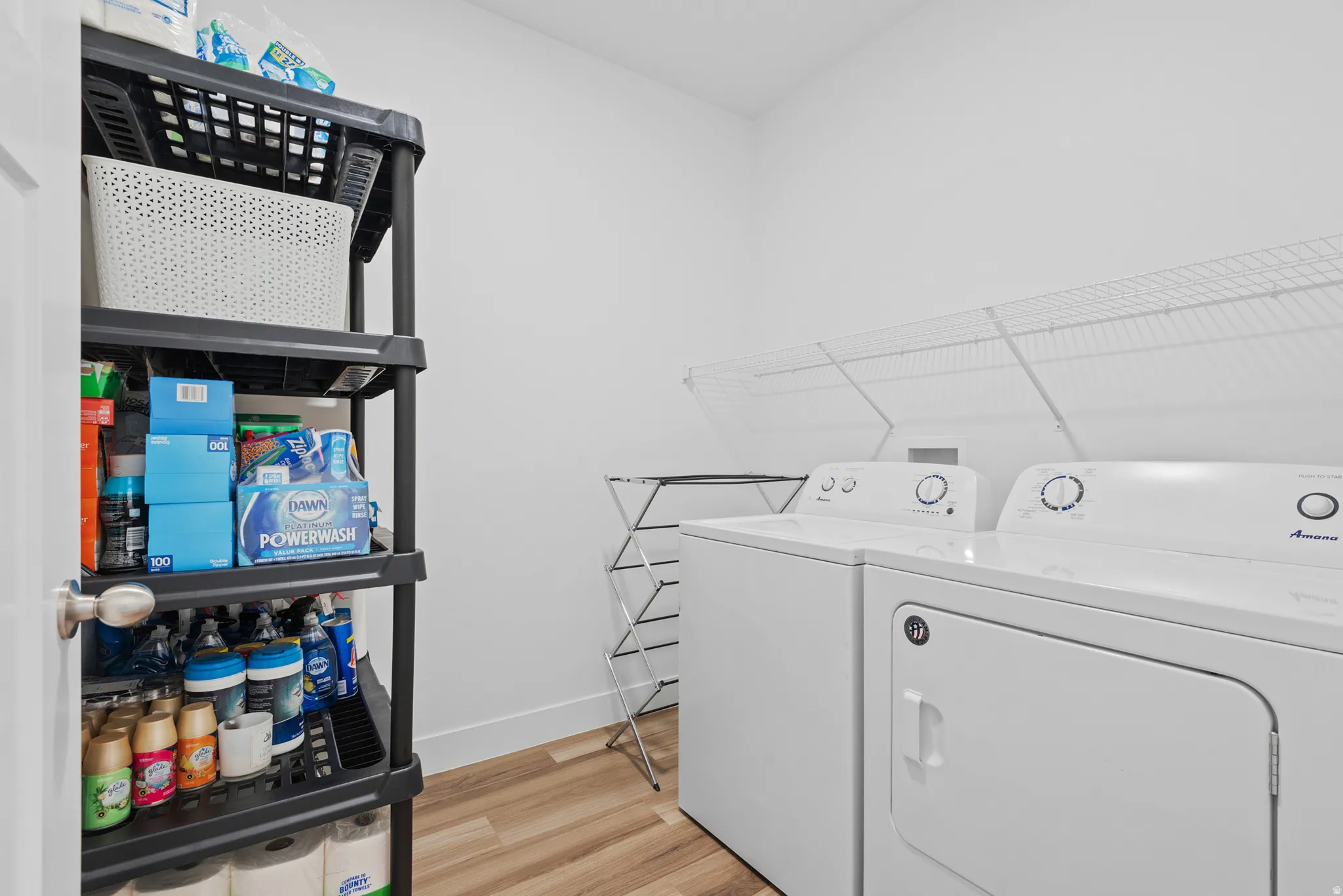 Laundry area with light wood-finish flooring, white walls, and a built-in wire shelf