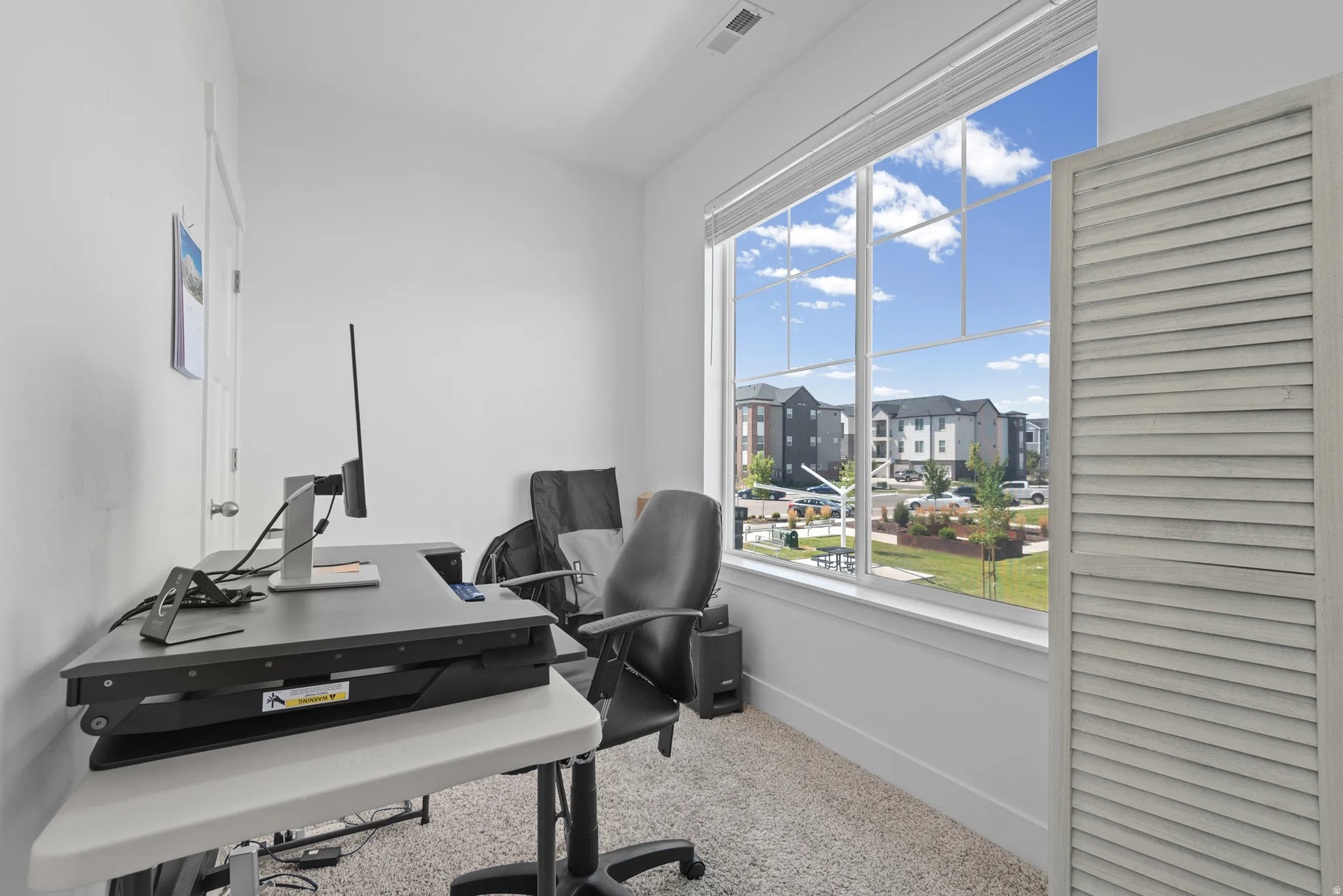 Room with broad window, white trim, and light-colored wall-to-wall carpeting