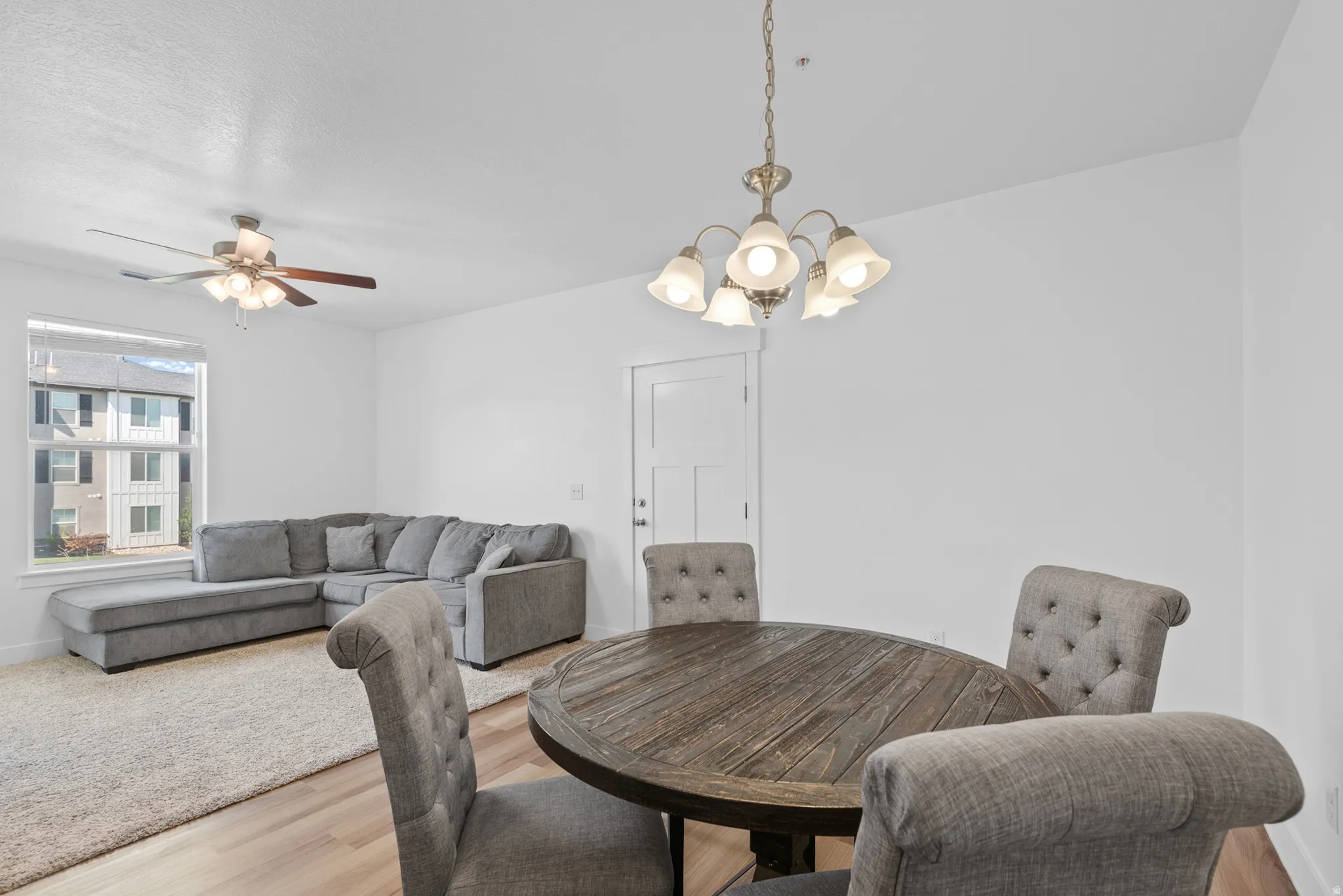 Open-concept living area featuring wood-finish flooring, a contemporary ceiling fan, and a multi-light chandelier