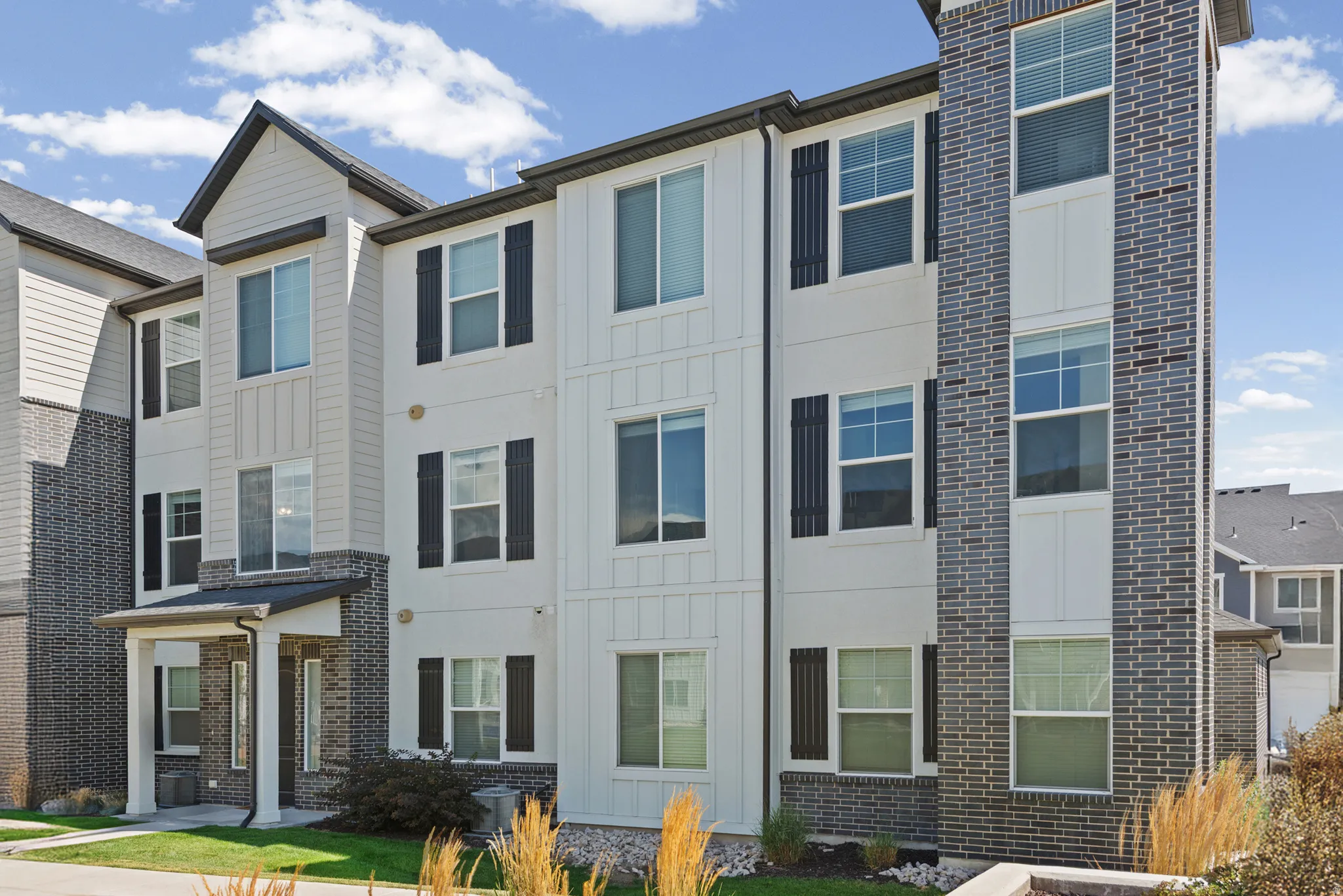 Three-story multi-family building with a prominent brick facade and contrasting vertical white siding