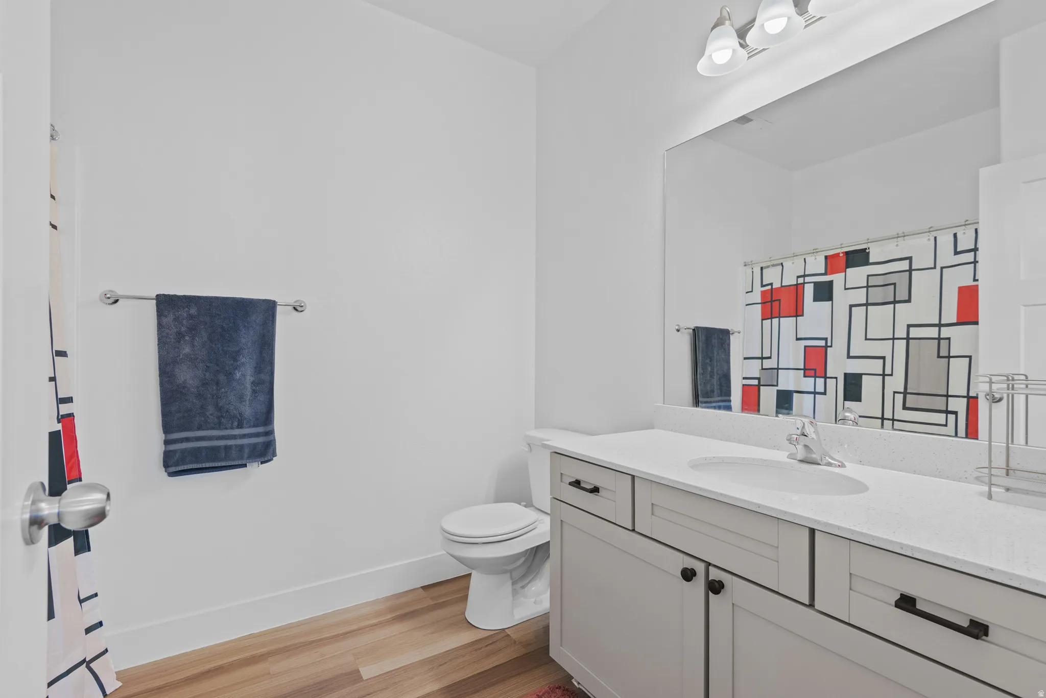 Bathroom featuring wood-finish flooring, a white vanity with integrated sink, a rectangular mirror, and a two-bulb vanity light fixture