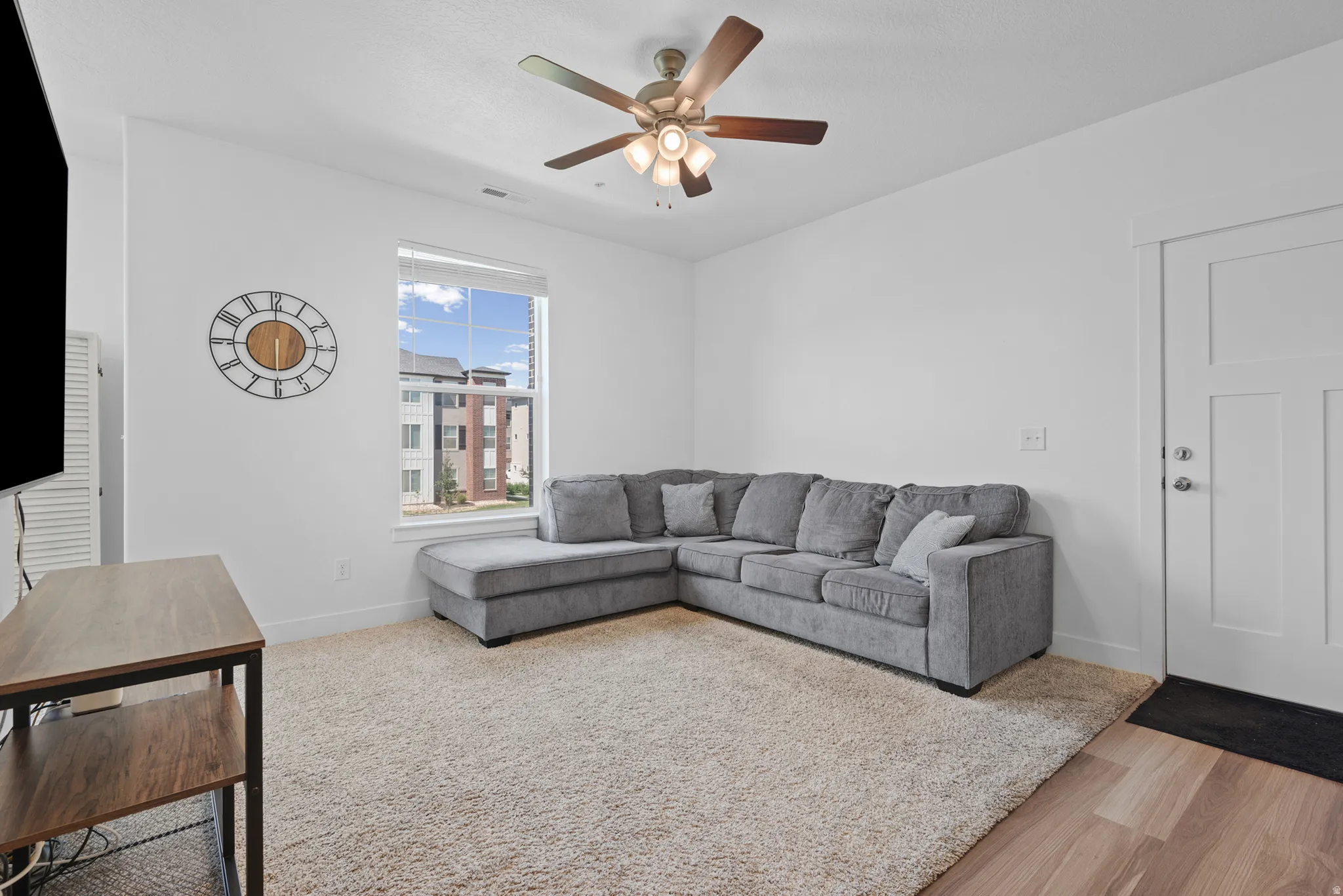Living area featuring a textured carpet, wood-finish flooring, a contemporary ceiling fan, and a bright window with exterior views