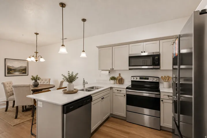 Kitchen featuring stainless steel appliances, light cabinetry, white countertops, and wood-finish flooring