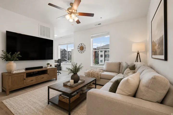 Bright living area with wood-finish flooring, a ceiling fan, and large windows