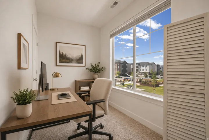 Expansive window with white trim, wood-finish desk with black metal frame, and light-colored carpet flooring