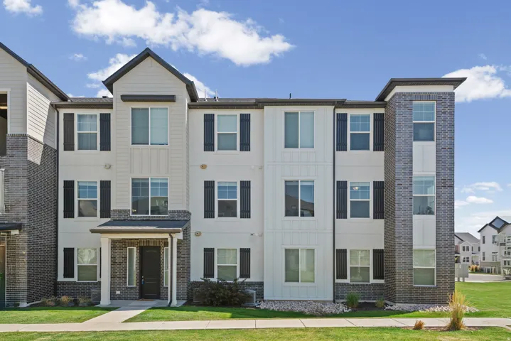 Multi-story exterior with a mixed-material facade featuring light-colored siding, dark brick accents, and black window shutters