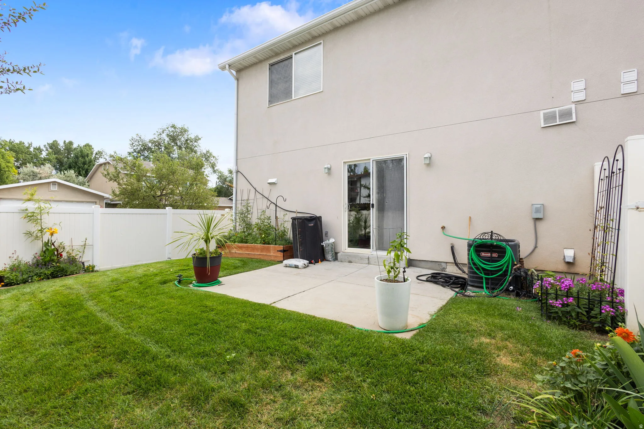 Expansive green lawn with a concrete patio, white vinyl fencing, and a sliding glass door providing exterior access