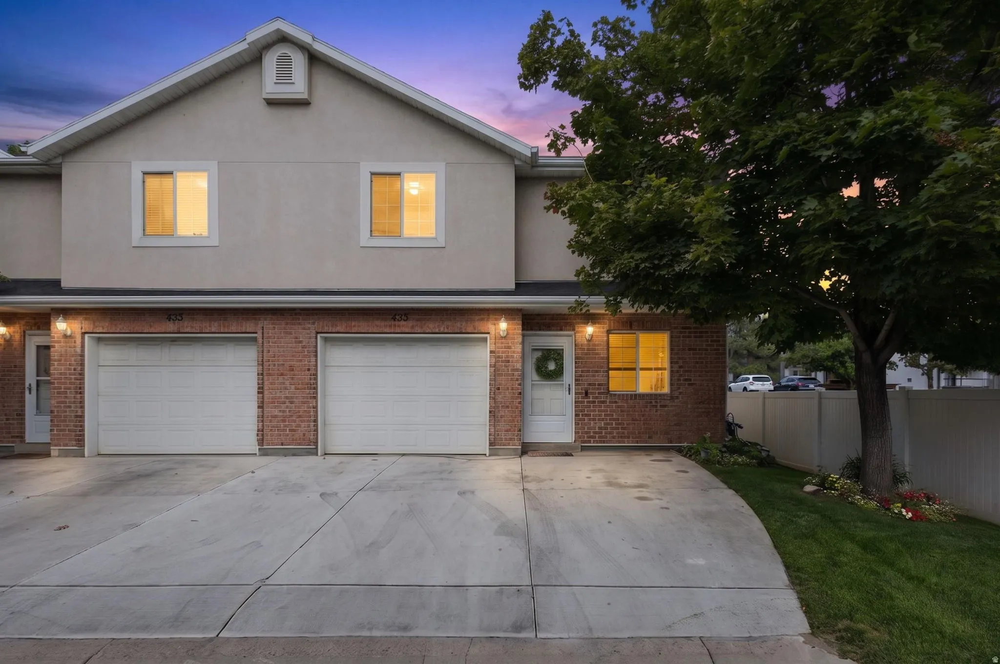 Brick and stucco townhouse exterior featuring two single-car garages, a private entry, and a mature tree