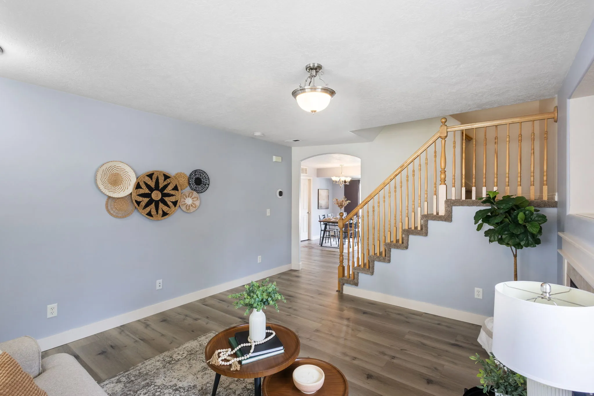 Open living area featuring wood-finish flooring, light blue wall paint, a staircase with wood balusters and carpeted treads, and an arched doorway leading to another room