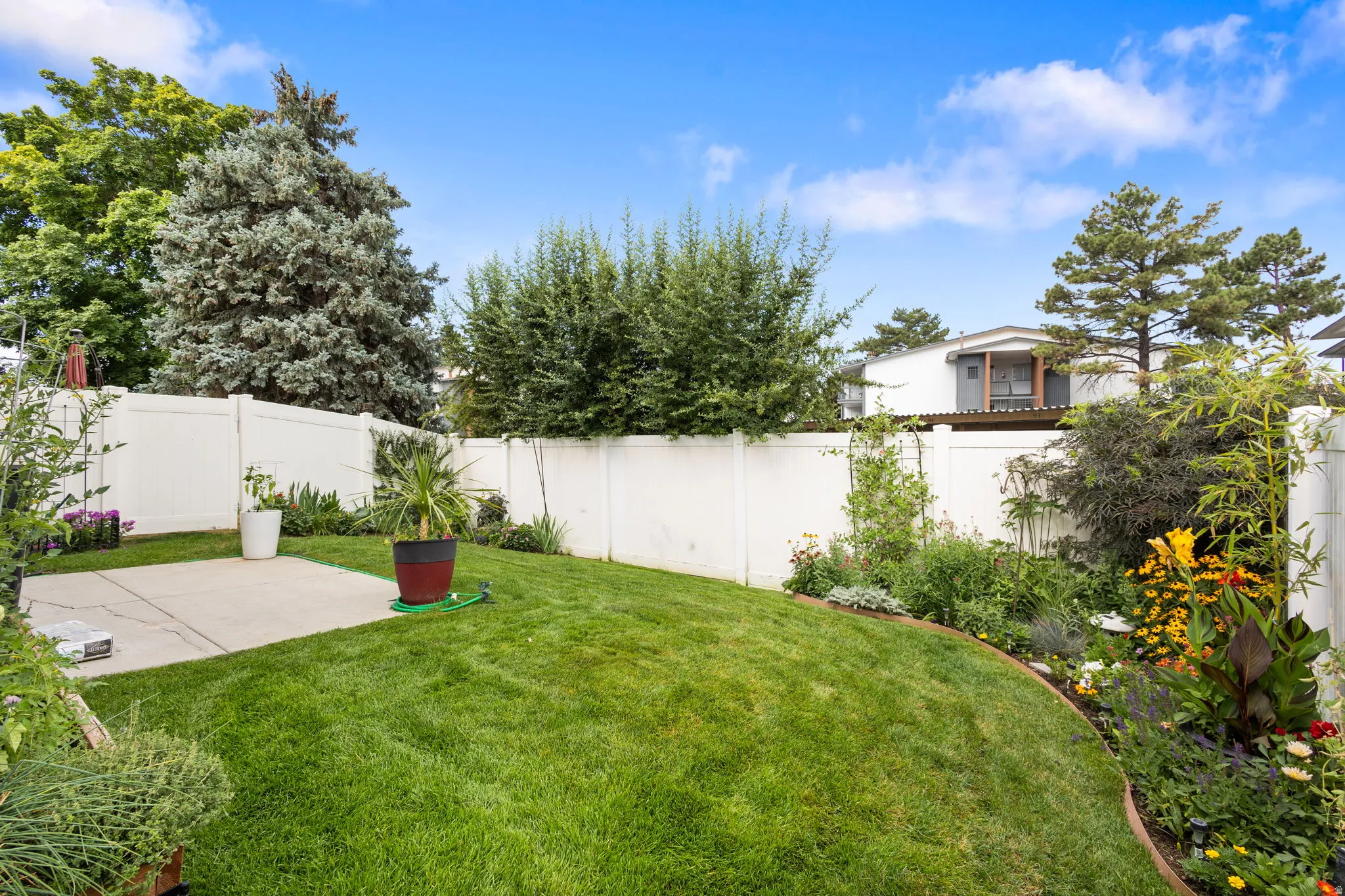 Manicured lawn with a concrete patio area, surrounded by a white privacy fence and mature landscaping