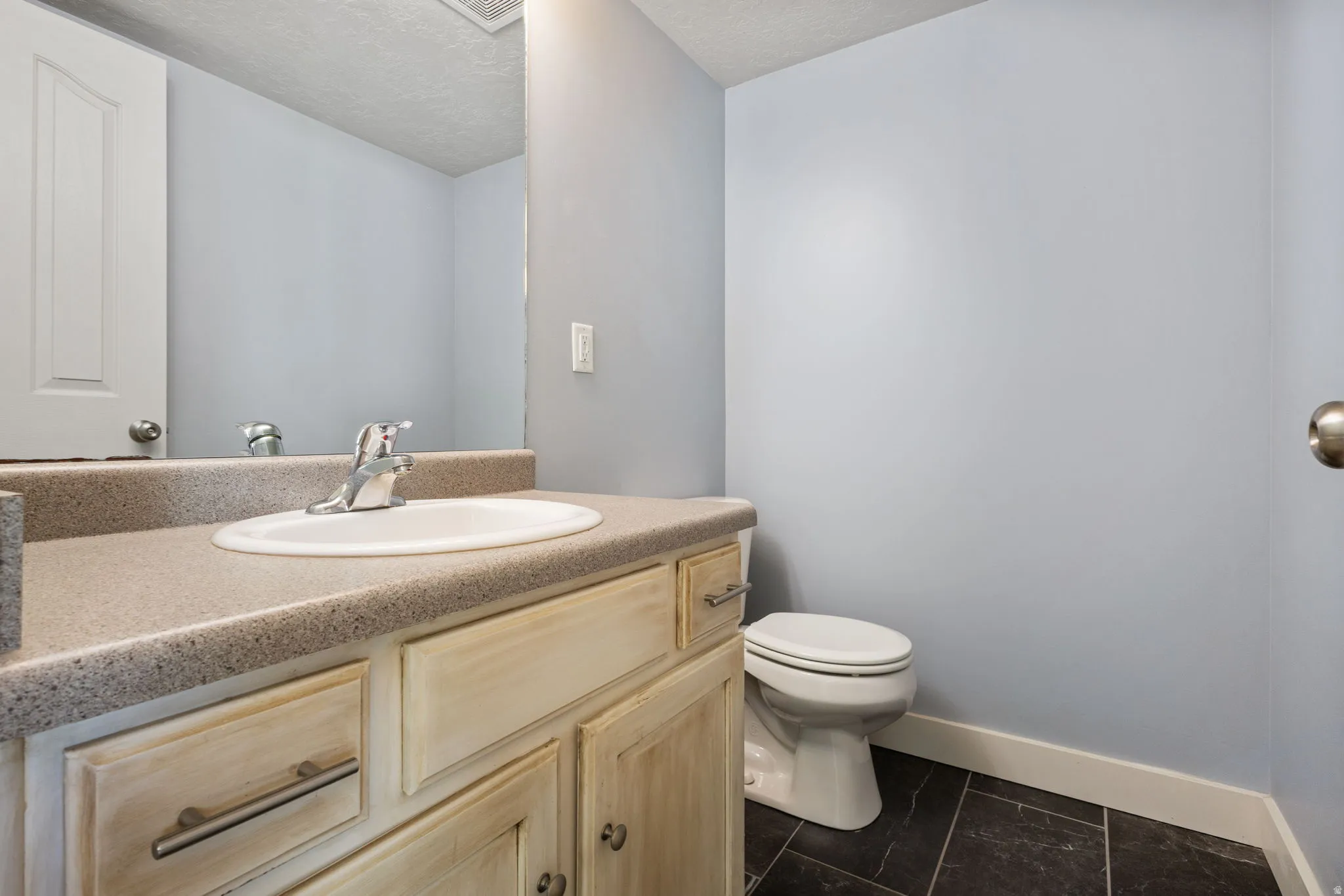 Bathroom featuring a light-toned vanity with an integrated sink, a dark countertop, and dark-toned tile flooring
