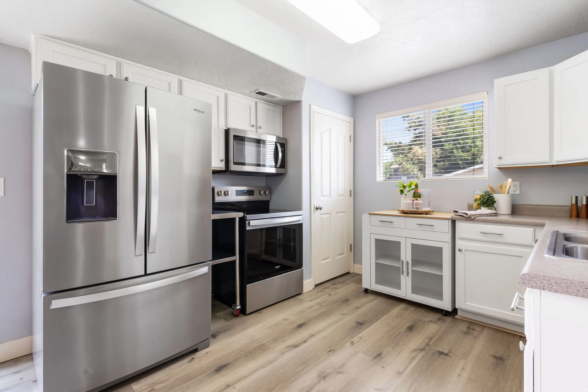 Kitchen featuring stainless steel appliances, white cabinetry, wood-finish flooring, and a window with horizontal blinds