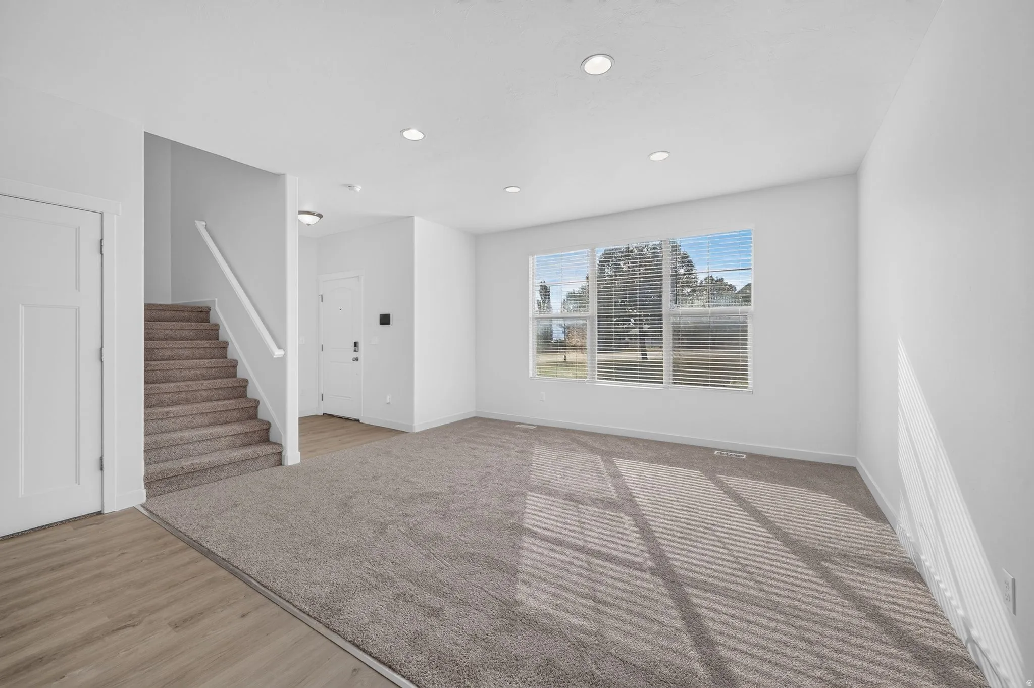 Spacious living area featuring neutral carpeting, recessed lighting, and large windows with blinds