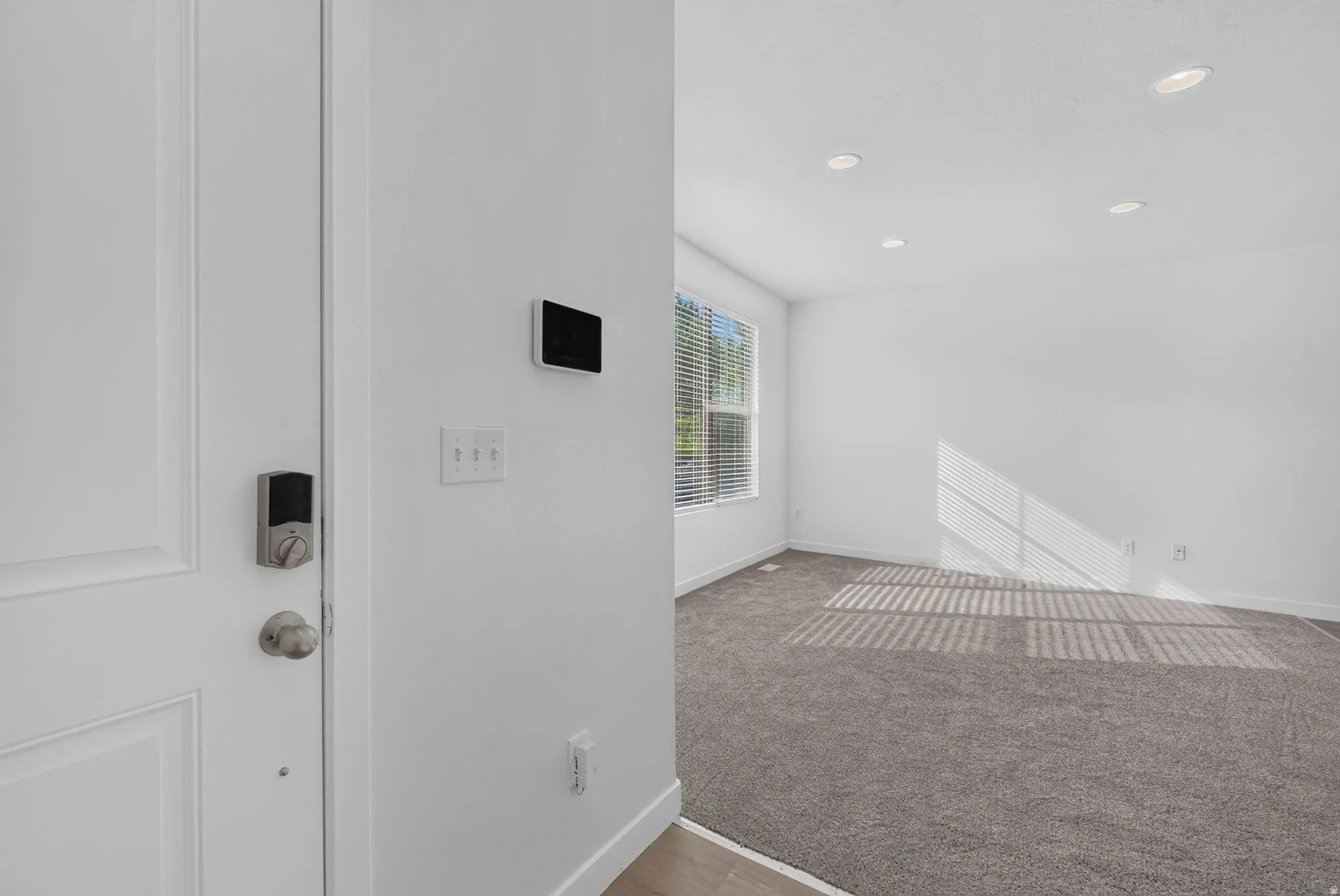 Entryway featuring a white paneled door with smart lock, light wood-finish flooring, and a wall-mounted smart home control panel