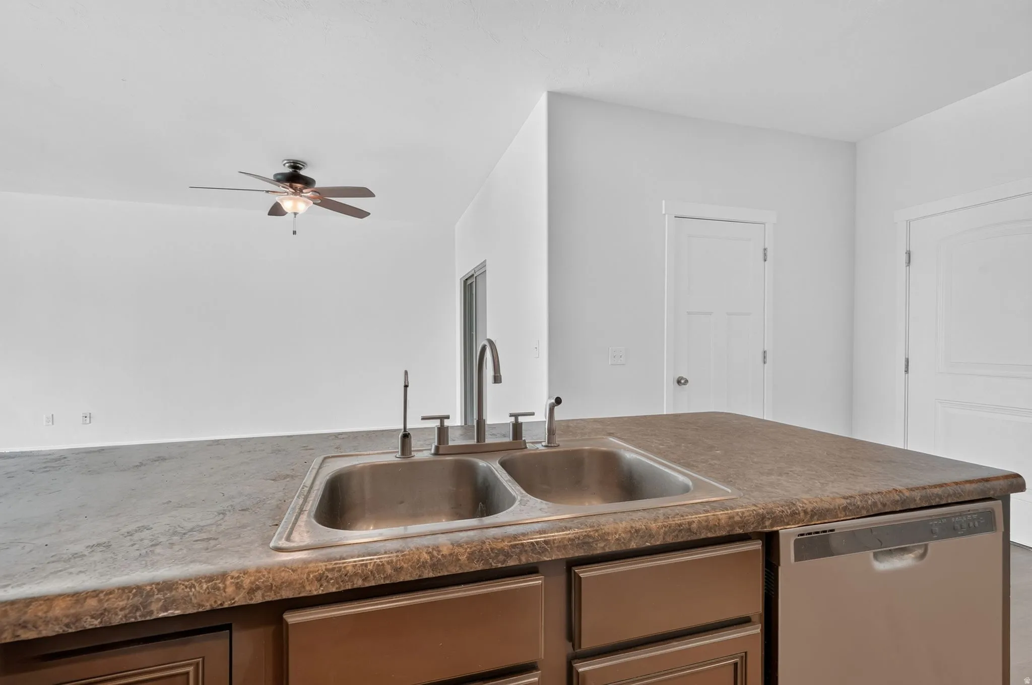Kitchen island featuring a double basin stainless steel sink with a high-arch faucet, a laminate countertop, and integrated dishwasher