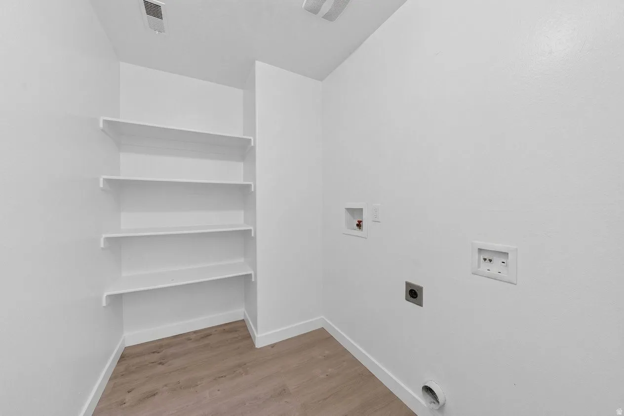 Dedicated utility space featuring built-in shelving, wood-finish flooring, white baseboards, and essential appliance hookups