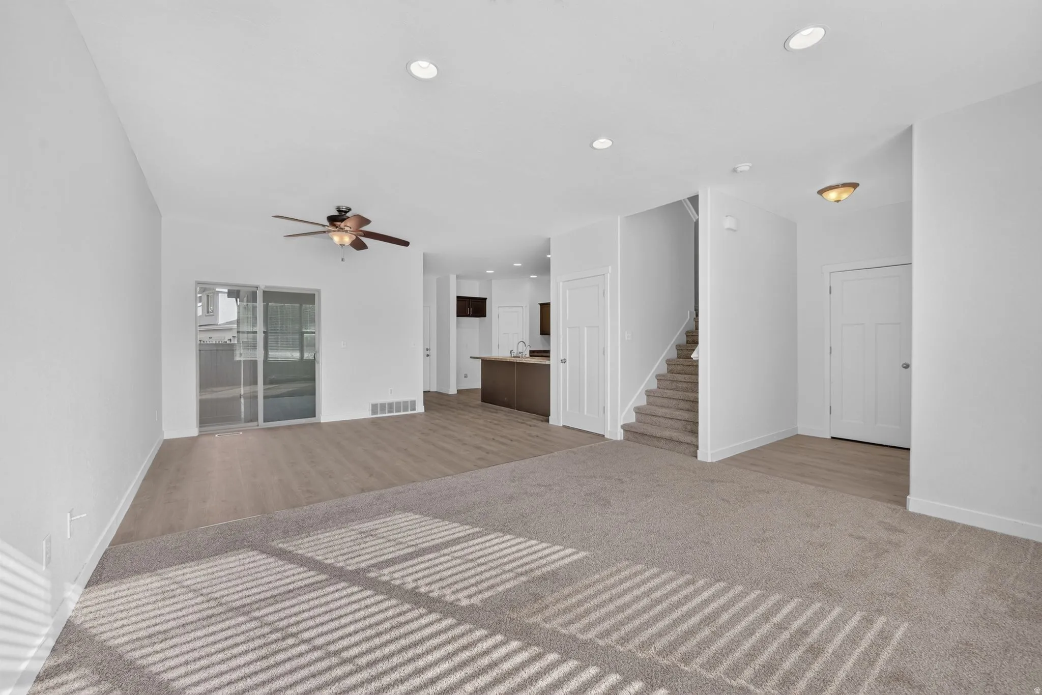 Expansive living area featuring light neutral wall paint and mixed flooring, with plush carpeting and wood-finish flooring