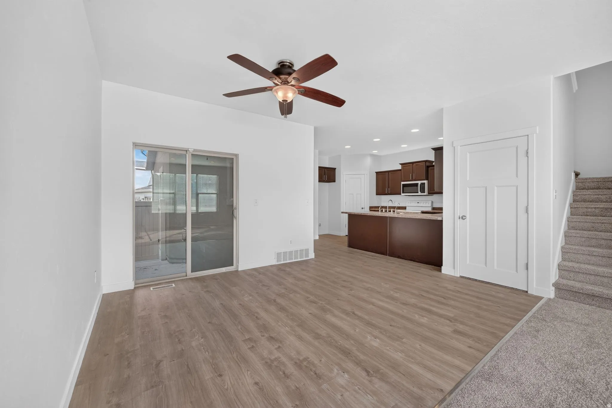 Open-concept living area featuring wood-finish flooring, a ceiling fan, and sliding glass doors