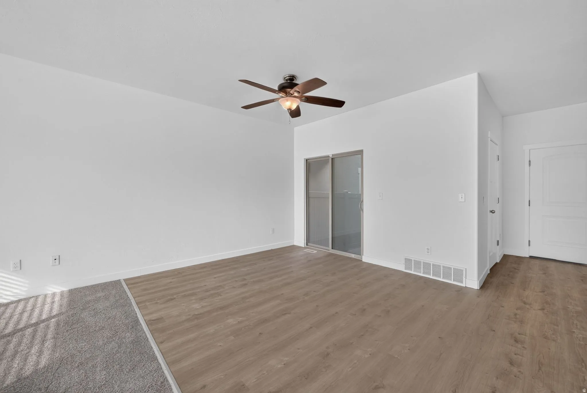 Spacious room featuring light wood-finish flooring, a ceiling fan with integrated lighting, and a sliding glass door