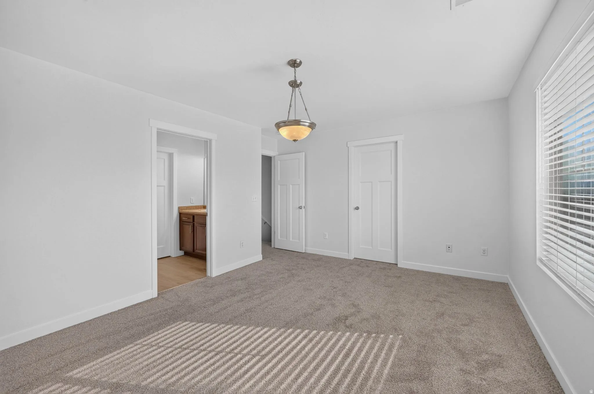 Spacious room featuring neutral carpeting, a modern pendant light fixture, and white trim throughout